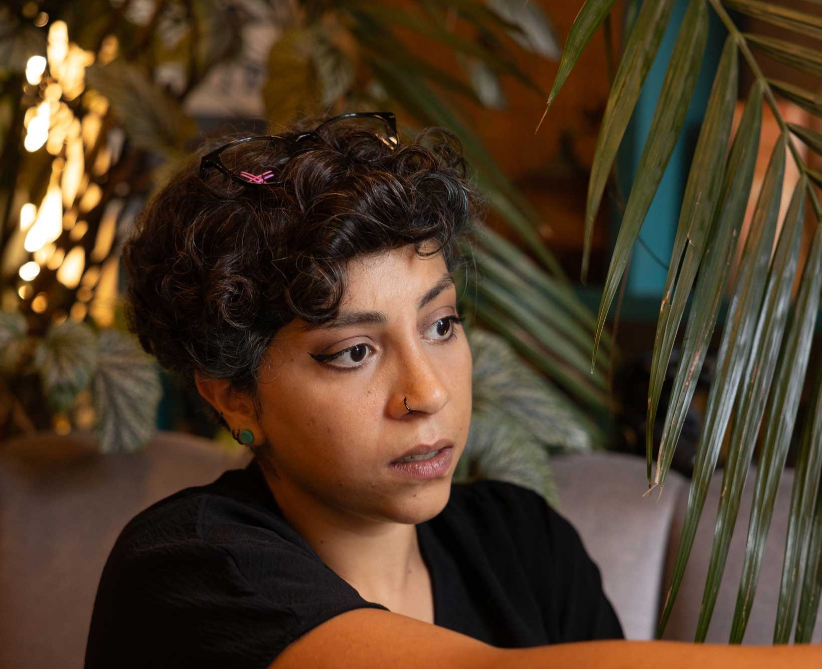 Person sitting at a table with plants and blurred lights in the background