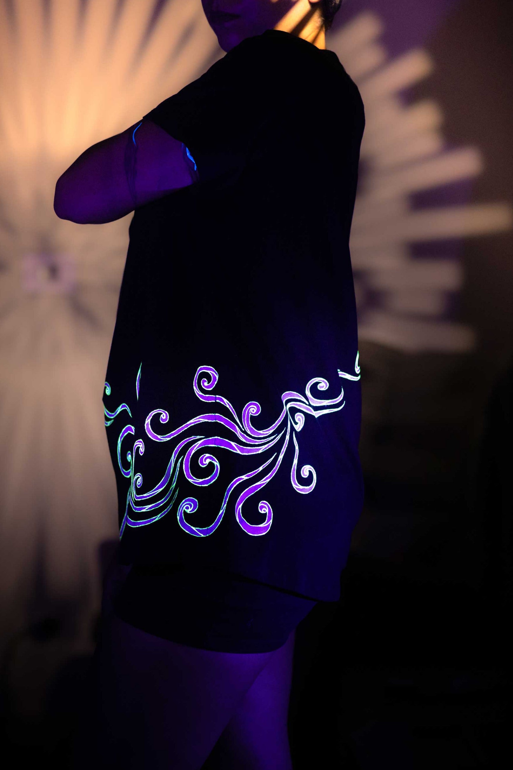 Person wearing a black shirt with glowing neon design in dark setting